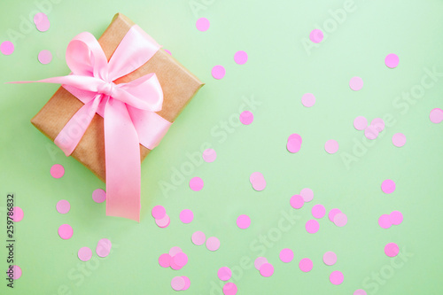 gift box pink ribbon on green paper background with pink confetti