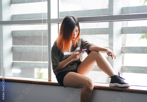 Asian highschool girl sitting by the window using smartphone