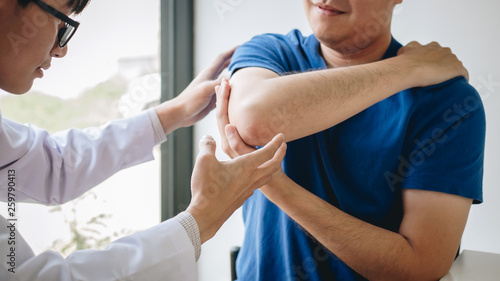 Doctor physiotherapist assisting a male patient while giving exercising treatment massaging the arm of patient in a physio room, rehabilitation physiotherapy concept