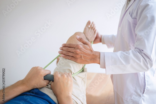 Doctor physiotherapist assisting a male patient while giving exercising treatment on stretching his leg on bed in the clinic