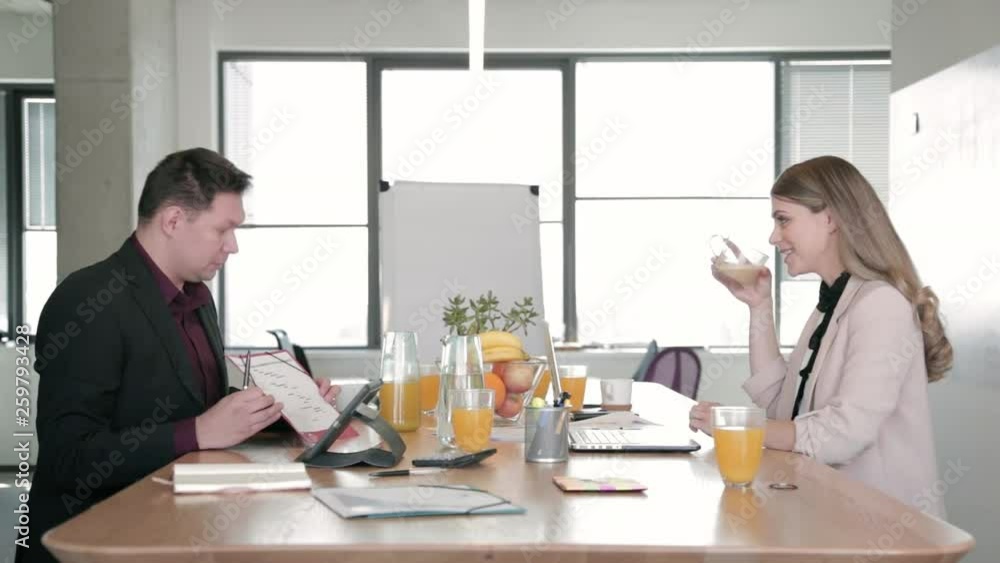 Static shot of two young business people sitting at the office desk, exchanging ideas, having fun, laughing and drinking coffee during a meeting. Static shot of two young business people sitting at the office desk, exchanging ideas, having fun, laughing and drinking coffee during a meeting.