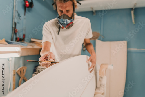 Man in respirator measuring surf board in workshop photo