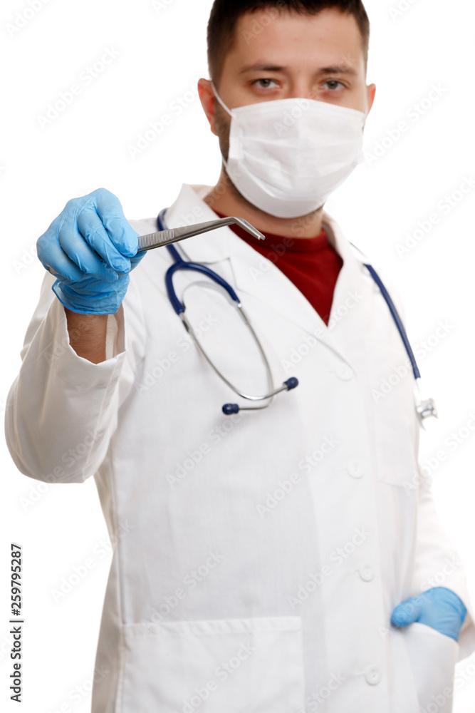 Photo of doctor in mask and white coat in rubber gloves holding tweezers. Photo of doctor in mask and white coat in rubber gloves holding tweezers.