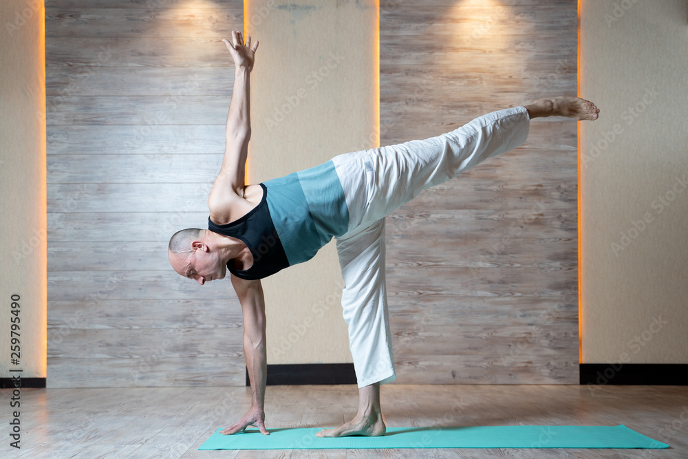 Athletic man standing leg doing yoga on blue mat.