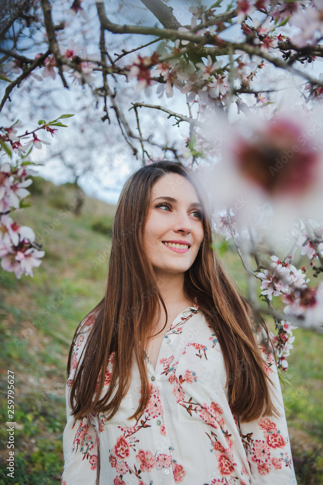 View through twigs of blooming wood of attractive cheerful lady looking away in garden between hills View through twigs of blooming wood of attractive cheerful lady looking away in garden between hills