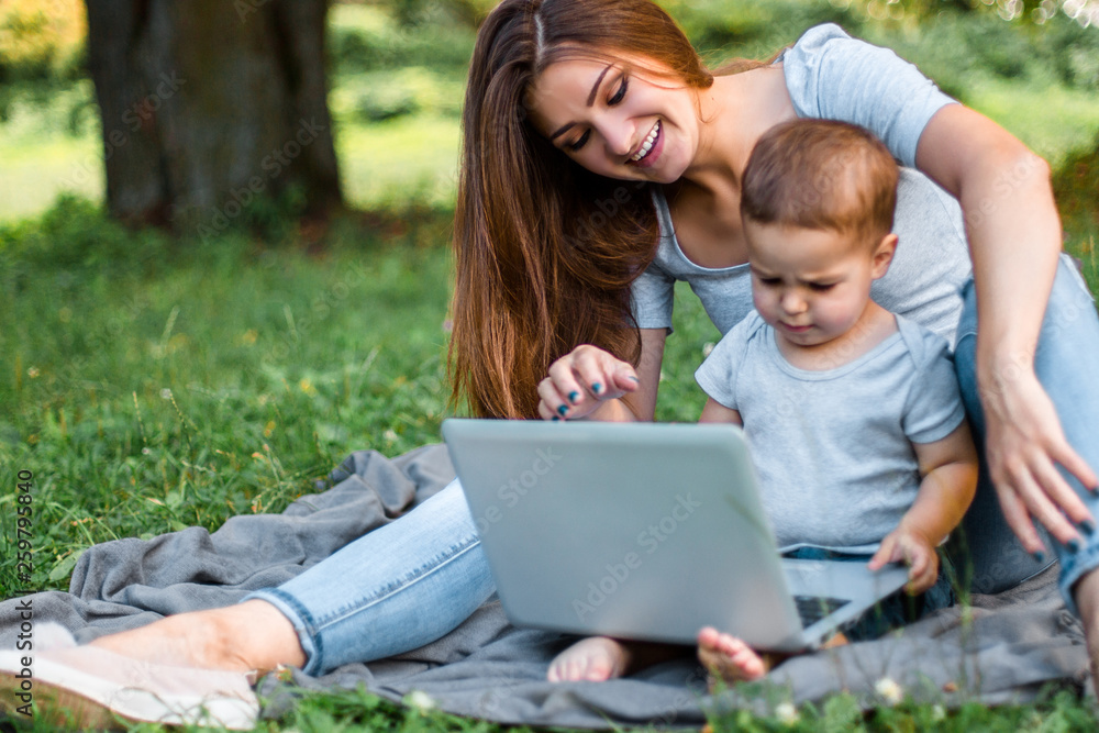 Mother with son sitting in the park and work on laptop. Mother with son sitting in the park and work on laptop.