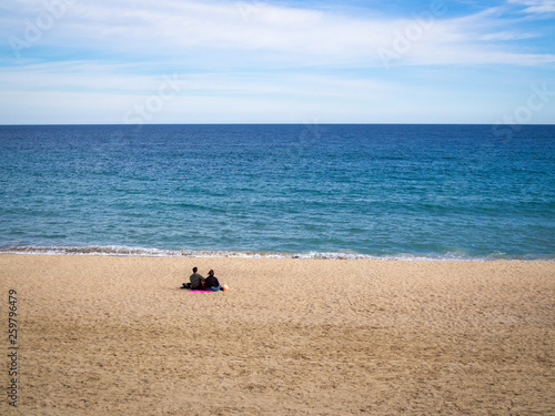 Lonely in love couple sitting on the beach in sunny day; copy space
