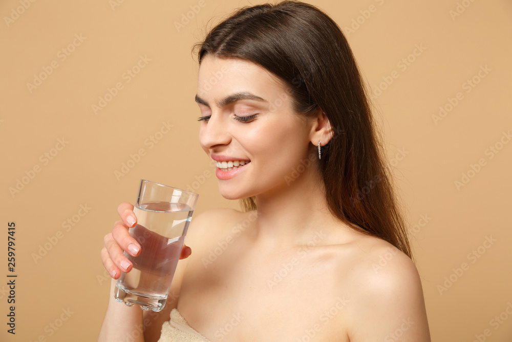 Close up brunette half naked woman 20s with perfect skin nude make up glass water isolated on beige pastel wall background, studio portrait. Healthcare cosmetic procedures concept. Mock up copy space. Close up brunette half naked woman 20s with perfect skin nude make up glass water isolated on beige pastel wall background, studio portrait. Healthcare cosmetic procedures concept. Mock up copy space.