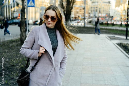 Beautiful young caucasian woman walking along the street in the city. Stylish female model swinging her hair in sunglasses walking on city street. © briagin