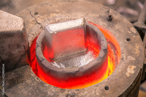 Closeup metal product melting in crucible on little foundry on blurred background