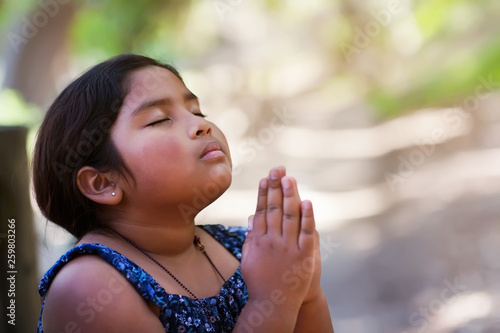 Φωτογραφία A young girl praying with hands together in reverence to God, wearing conservative clothing and in an outdoor setting