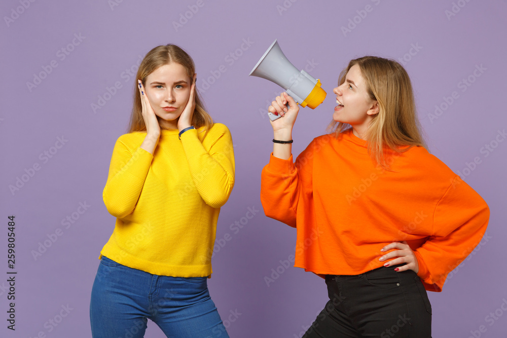 Two young blonde twins sisters girls in colorful clothes covering ears with hands, scream on megaphone isolated on pastel violet blue background. People family lifestyle concept. Mock up copy space. Two young blonde twins sisters girls in colorful clothes covering ears with hands, scream on megaphone isolated on pastel violet blue background. People family lifestyle concept. Mock up copy space.