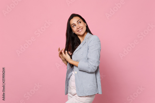 Portrait of smiling pretty dreamful young woman in striped jacket holding hair and looking aside isolated on pink pastel wall background. People sincere emotions lifestyle concept. Mock up copy space. © ViDi Studio