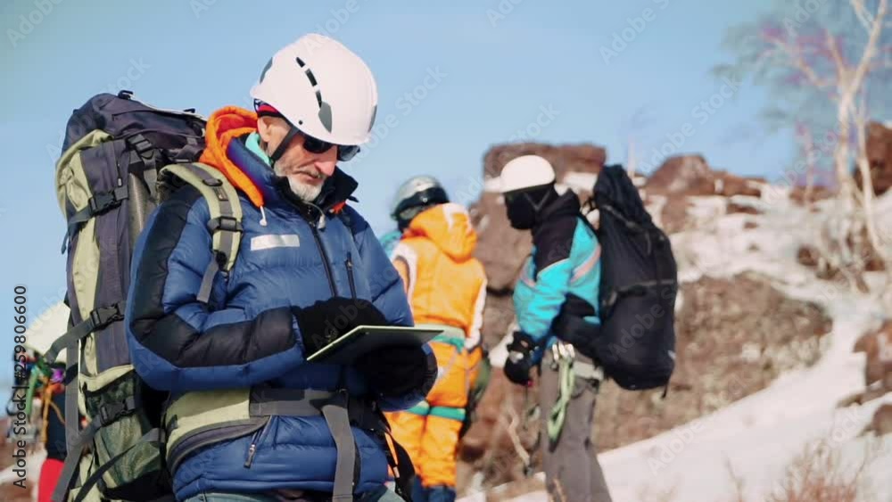 An experienced climber with the white beard and sunglasses is at rest and looking at tablet the way An experienced climber with the white beard and sunglasses is at rest and looking at tablet the way