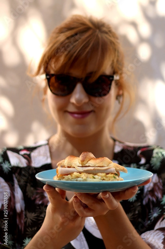 Young woman holding a plate with croissant  egg  ham and cheese sandwich. Selective focus.