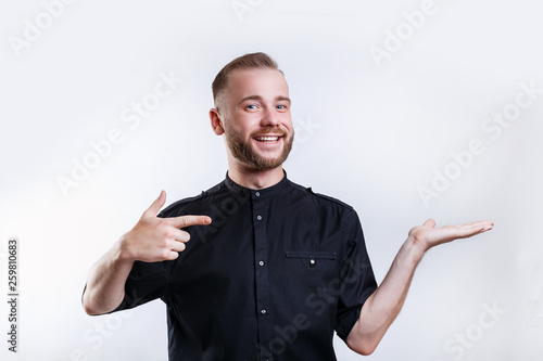 Portrait of a joyful young man pointing fingers away at copy space on his palm over white background