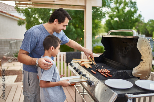 father teaching son how to grill hot dogs and bonding photo