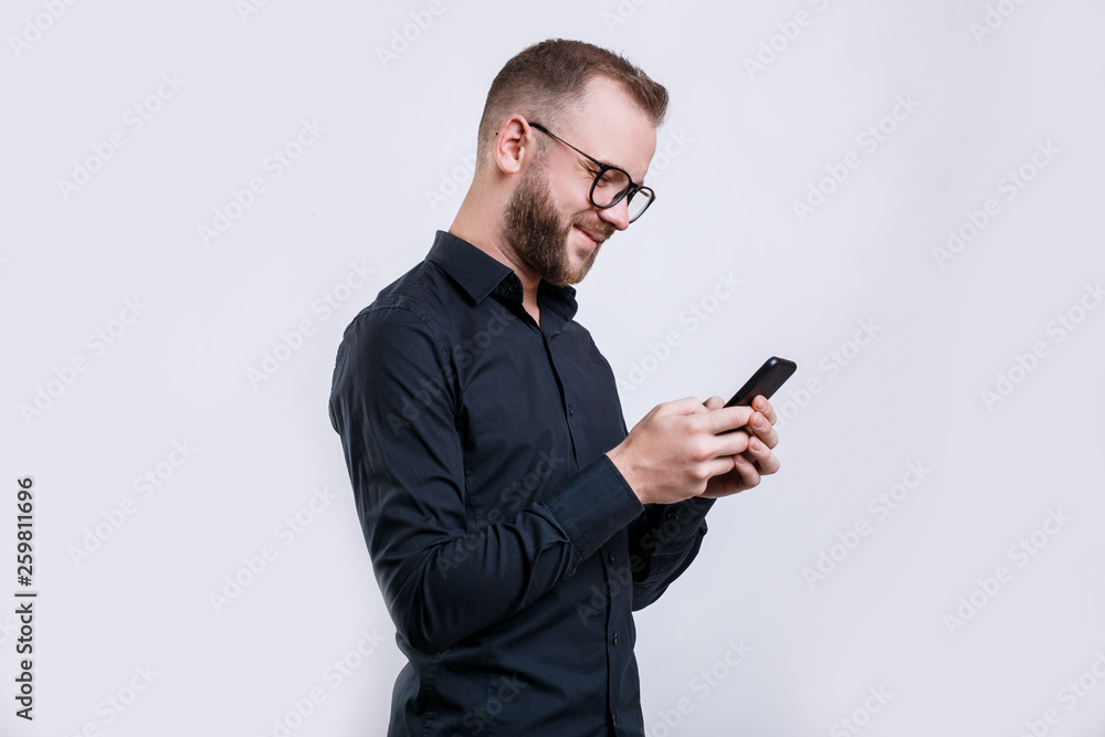 Portrait of young bearded caucasian man in glasses looking at mobile phone over white background, Portrait of young bearded caucasian man in glasses looking at mobile phone over white background,