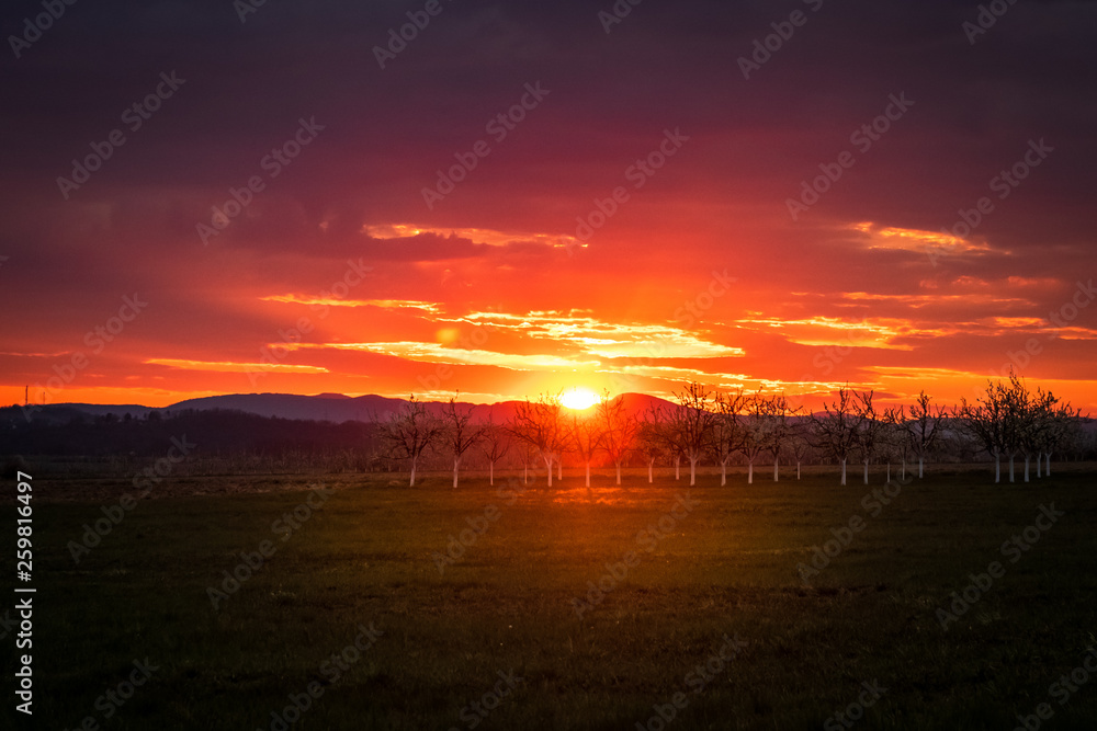 Beautiful colorful sunset with orange cloud sky. Rural landscape with hills and mountains.