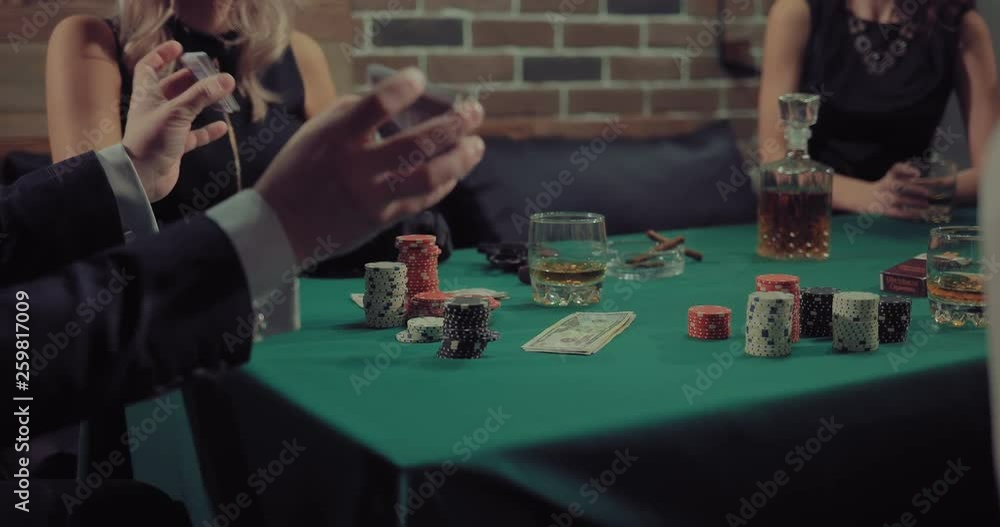 Man mixes and distributes a deck of cards. Company plays poker. Gaming chips, money, cigars and whiskey lie on a green table. Man mixes and distributes a deck of cards. Company plays poker. Gaming chips, money, cigars and whiskey lie on a green table.