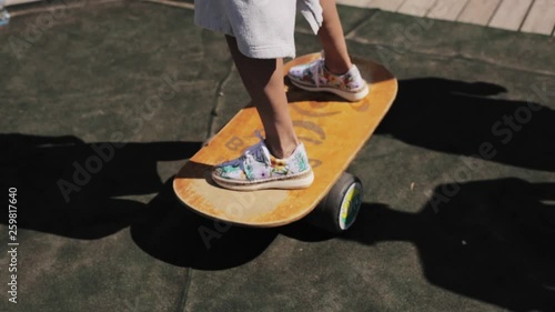 Woman's legs wearing cute sportive sneakers are standing on yellow wooden balance board on sunny warm summer day at concrete platform.