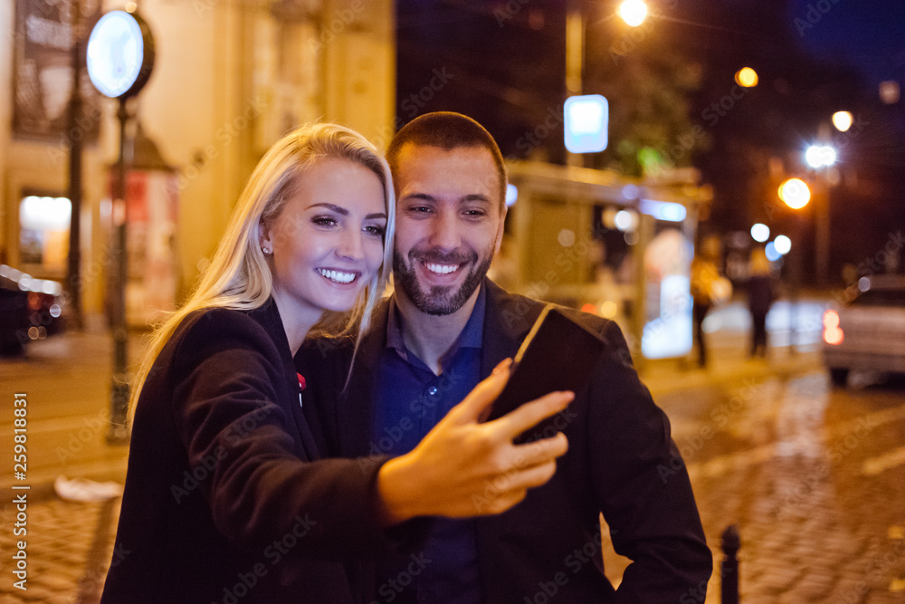 Happy couple taking selfie in the city at dusk