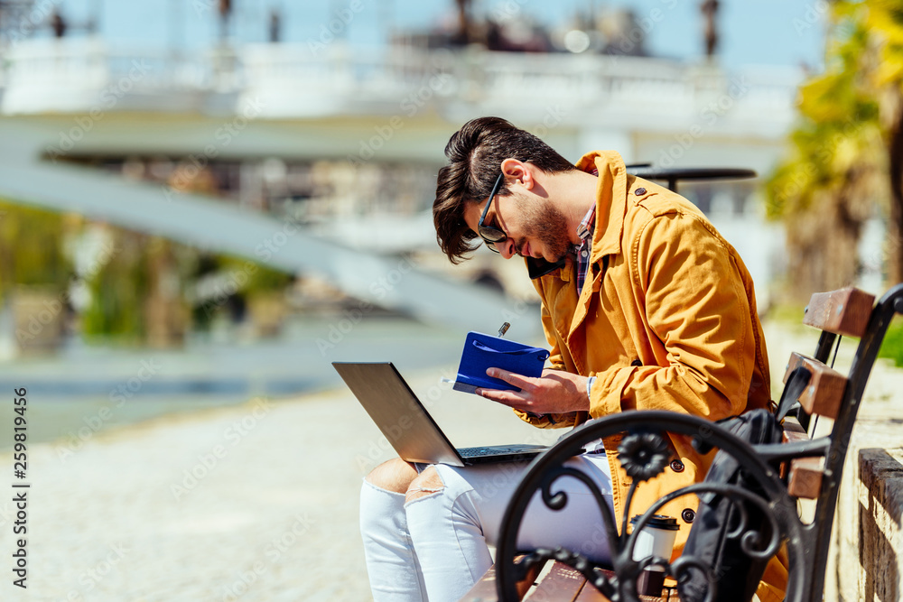 Urban businessman writing in notebook and using his laptop Urban businessman writing in notebook and using his laptop