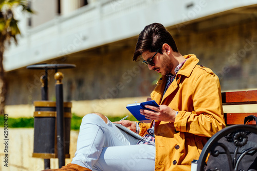 Attractive businessman in yellow coat writing in notebook