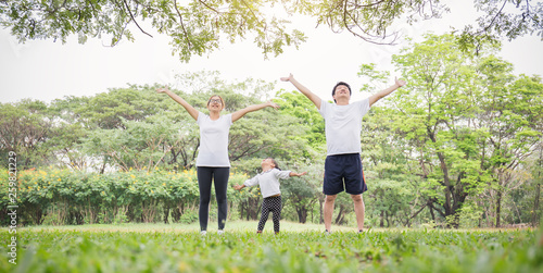 Family exercising and jogging together breathing fresh air at the park. Group of asian family father mother and daughter girl stretching after sport on the grass. Sport health care concept banner.