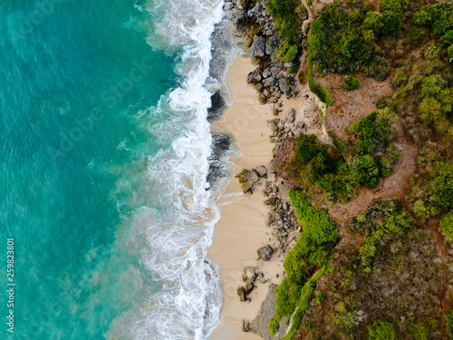 Aerial view sand beach with rocks and green cliff, top view of a beautiful sandy beach with rocks and waves, aerial shot with the blue waves rolling into the shore, some rocks present