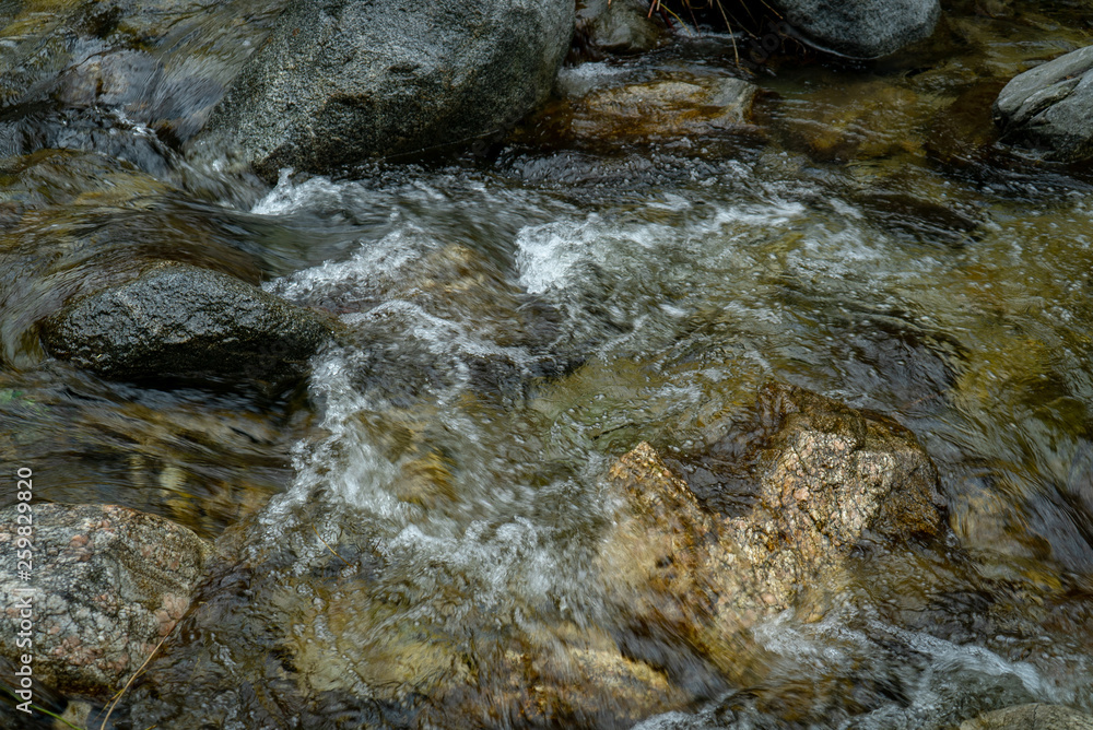 Low angle view of rocks in shallow stream with water flowing and bubbling over and around them.