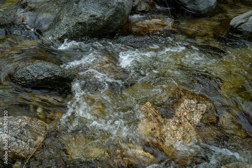 Low angle view of rocks in shallow stream with water flowing and bubbling over and around them.