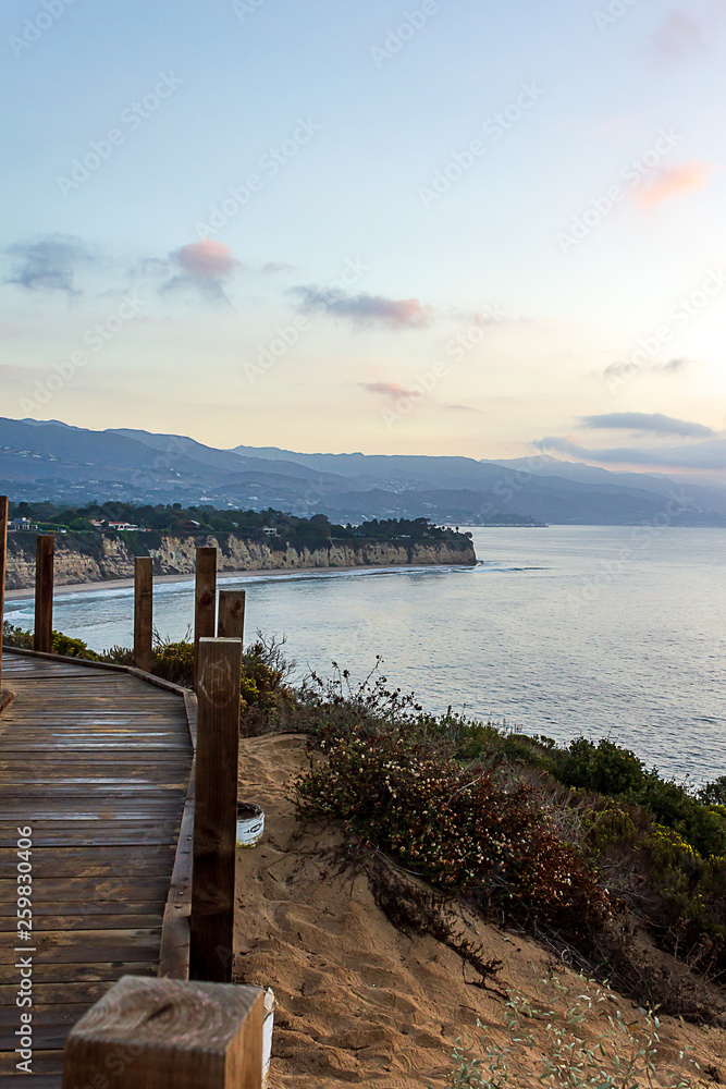 Fototapeta premium cliff side view of pacific ocean with boardwalk trail, plants and distant mountains