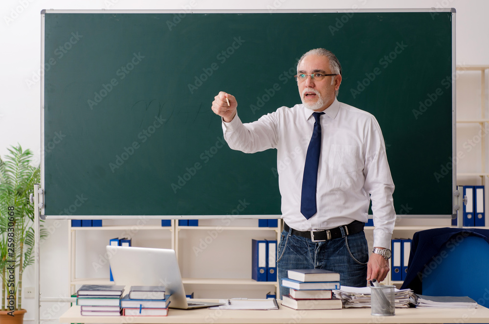 Aged male teacher in front of chalkboard Aged male teacher in front of chalkboard