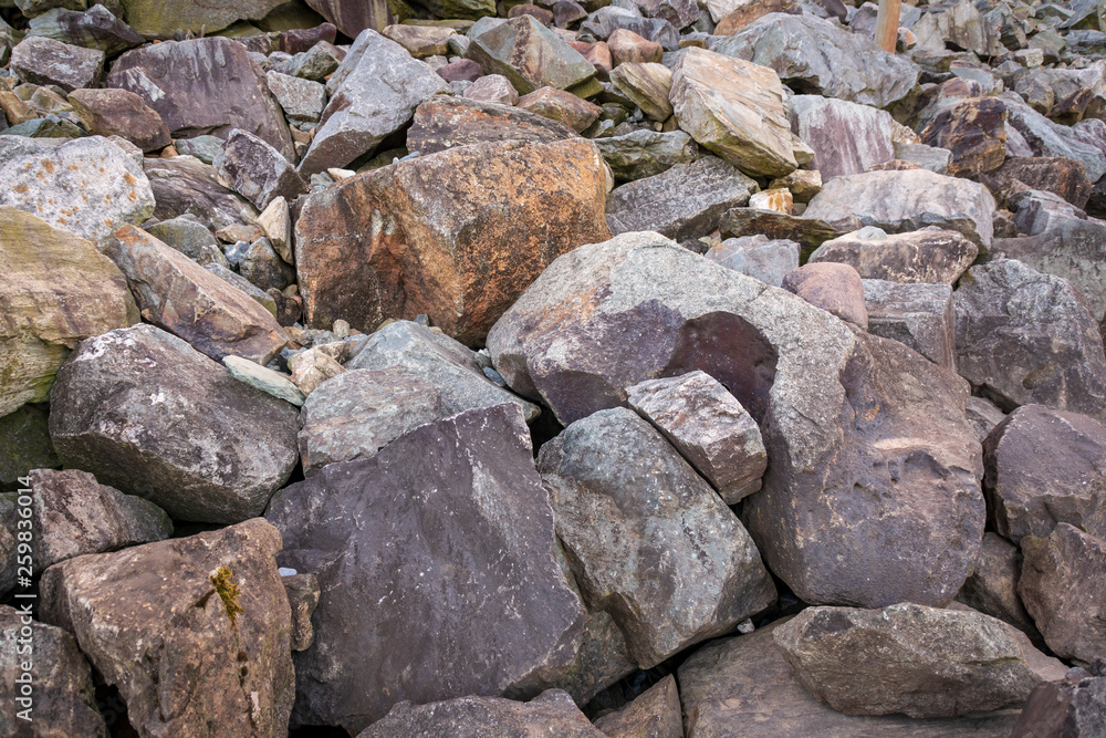 Heavy rocks and boulders of different shades of greys and browns lay piled on a hill.
