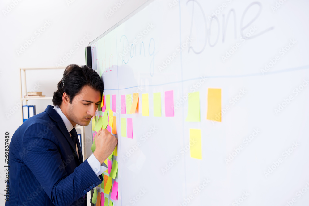 Young handsome employee in front of whiteboard with to-do list Young handsome employee in front of whiteboard with to-do list