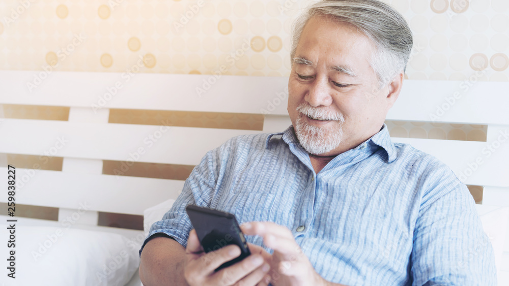Senior Male using a smartphone , smiling feel happy in bed at home - lifestyle senior concept Senior Male using a smartphone , smiling feel happy in bed at home - lifestyle senior concept