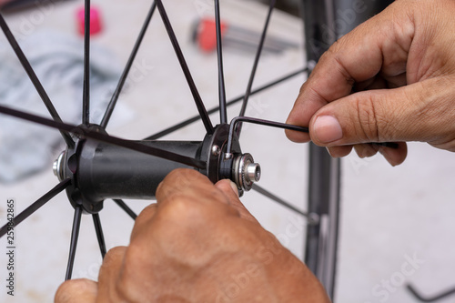 Technician man hand repairing and adjust the bicycle wheel bearing by hex key. Maintenance concept.