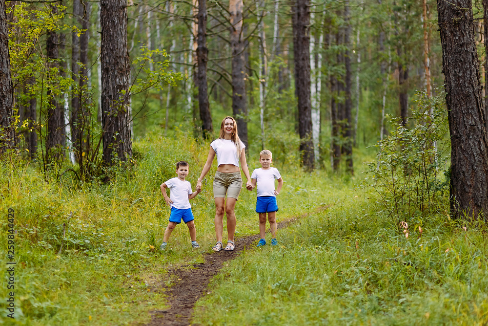 Fototapeta premium young slender mom and two preschoolers children in white t-shirts holding hands in the summer