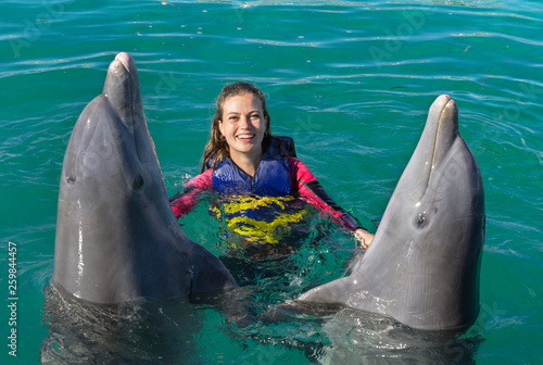 Photography Smiling woman swimming with dolphins in blue water.