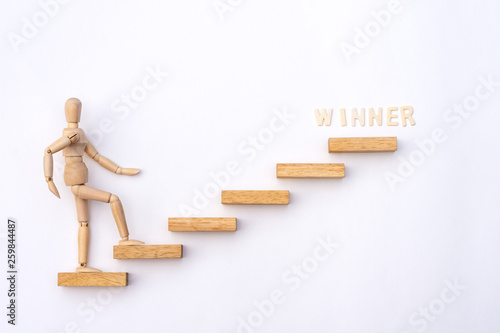 Ascending stairs and wooden man model going upward to words"WINNER' on white background.Business growth, steps to success or progress way to forward achievement concept. 