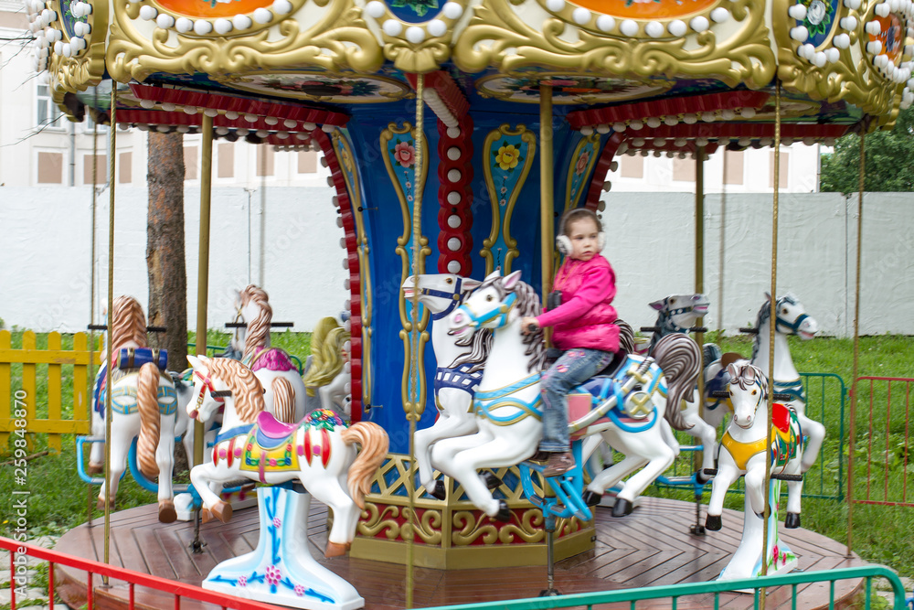 a little girl on a children's carousel in the city Park