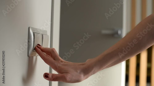 Female hand turning off the light switch. Close-up shot. Door on Background