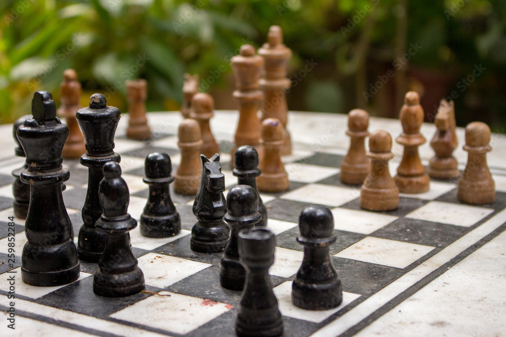Outdoor chessboard with black and yellow figures with unfocused background. Competition and strategy concept. Intelligent sport. Defeat and fight concept. Chess wooden pieces on board. 
