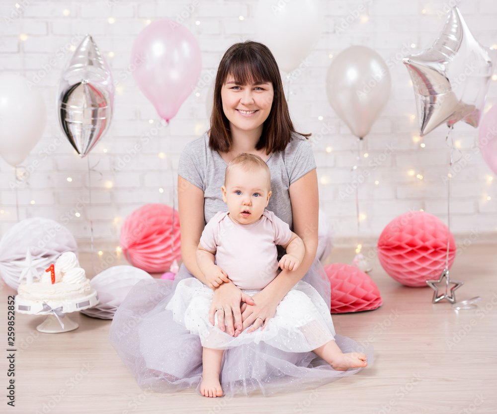 first birthday - beautiful girl with mother in decorated room with cake and balloons over white wall first birthday - beautiful girl with mother in decorated room with cake and balloons over white wall