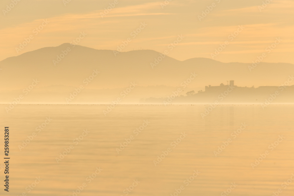 Beautiful view of Trasimeno lake at sunset with birds on water and Castiglione del Lago town Beautiful view of Trasimeno lake at sunset with birds on water and Castiglione del Lago town