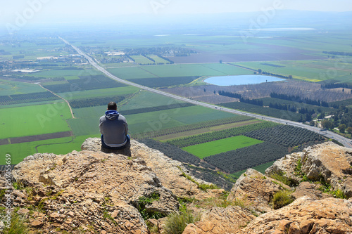 lonely man sits on the edge of a cliff and looks at the magnificent landscape of the Jezreel Valley, neighborhood Nazareth, Lower Galilee, Israel