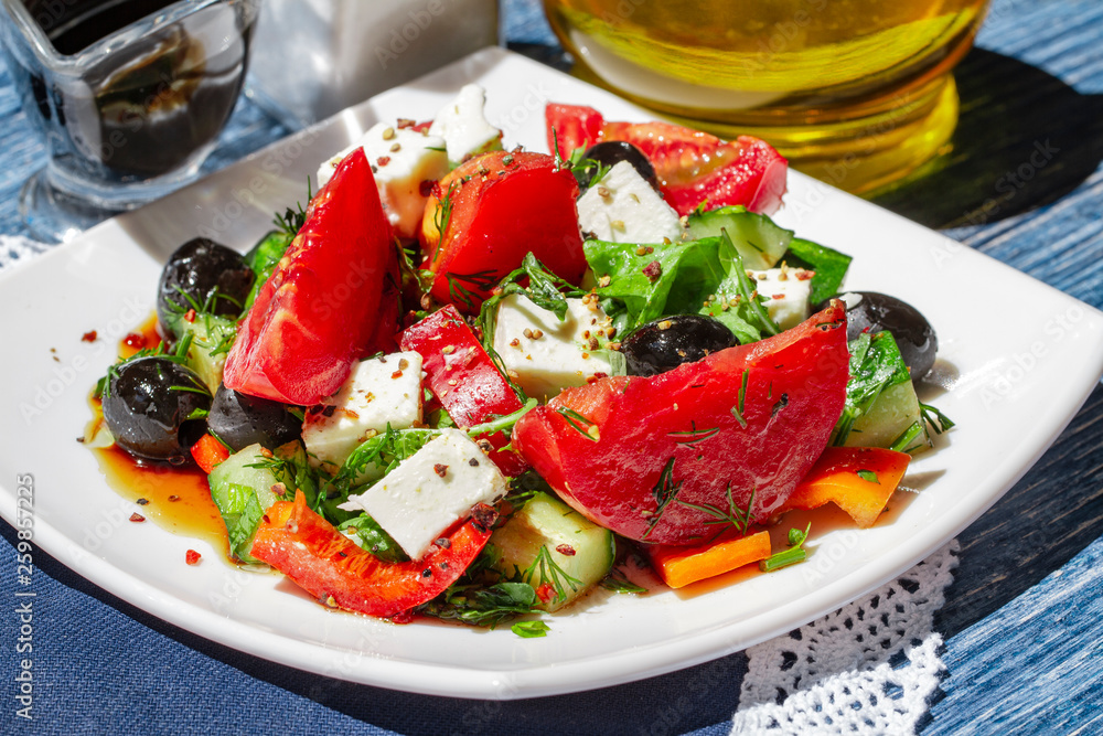 Greek salad of fresh cucumbers, tomatoes, sweet peppers, lettuce, feta cheese and olives with olive oil, balsamic vinegar and sea salt. bright daylight Mediterranean style photo. Healthy summer food.