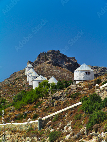 Beautiful traditional white windmills on a hill in Leros island, Greece. Medieval castle on hill top.