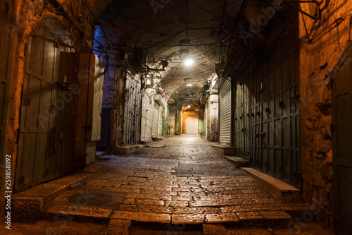 Narrow cobbled street in old medieval town with illuminated houses and pavement. Night shot of side passage in some ancient castle. Closed doors, stone paving and hanging lights in the street.